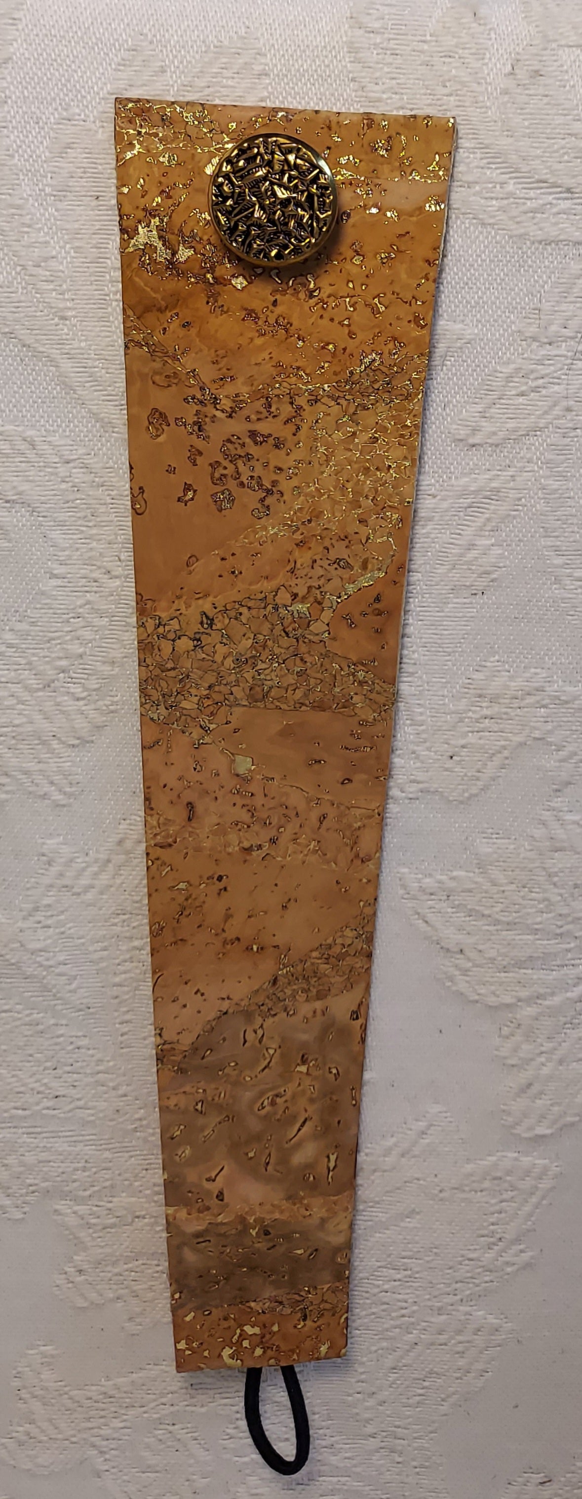 Flat view of gold-flecked natural cork bracelet with a gold button clasp, highlighting its unique texture and sustainable material.